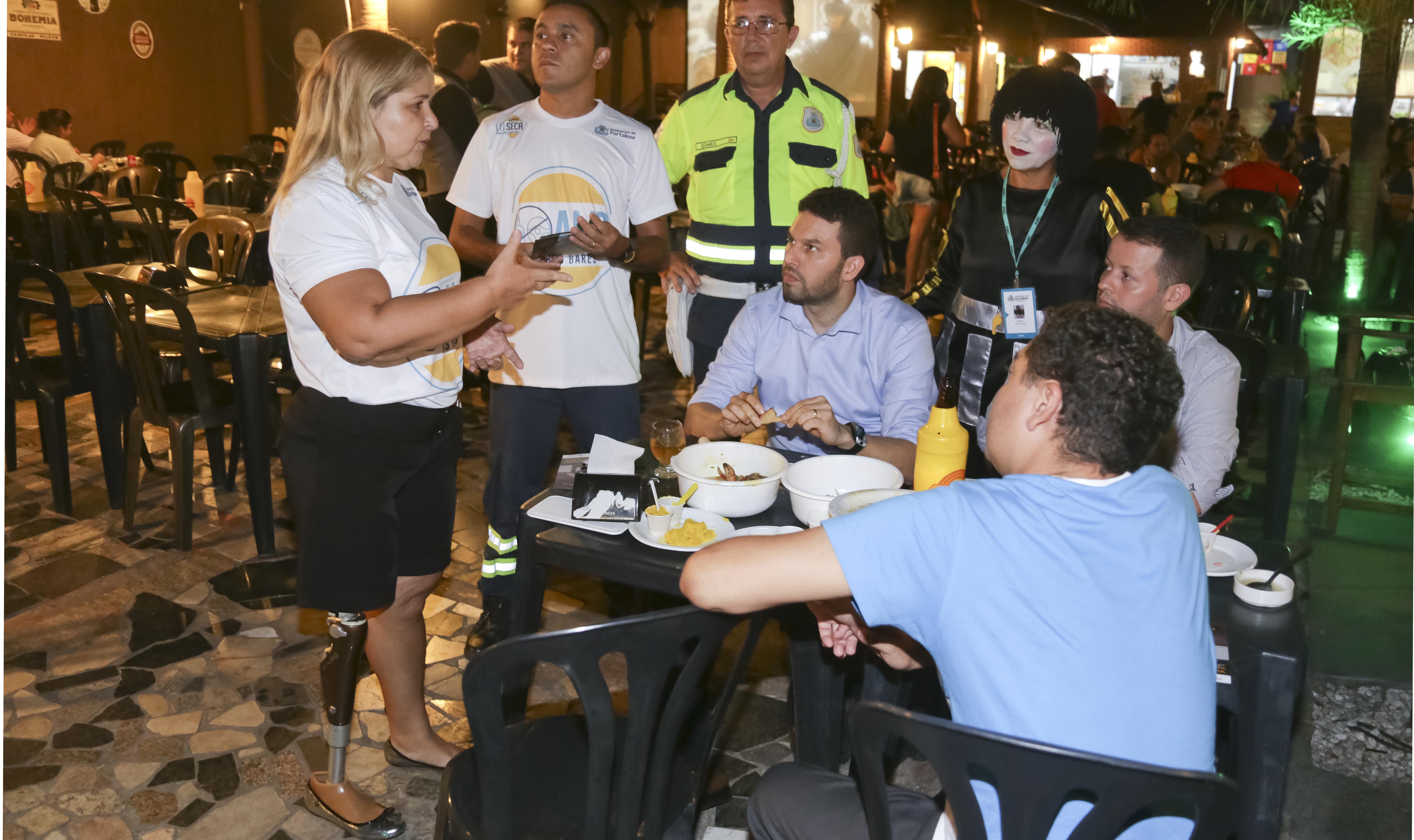 agentes da AMC abordam pessoas numa mesa de bar sobre campanha da lei seca